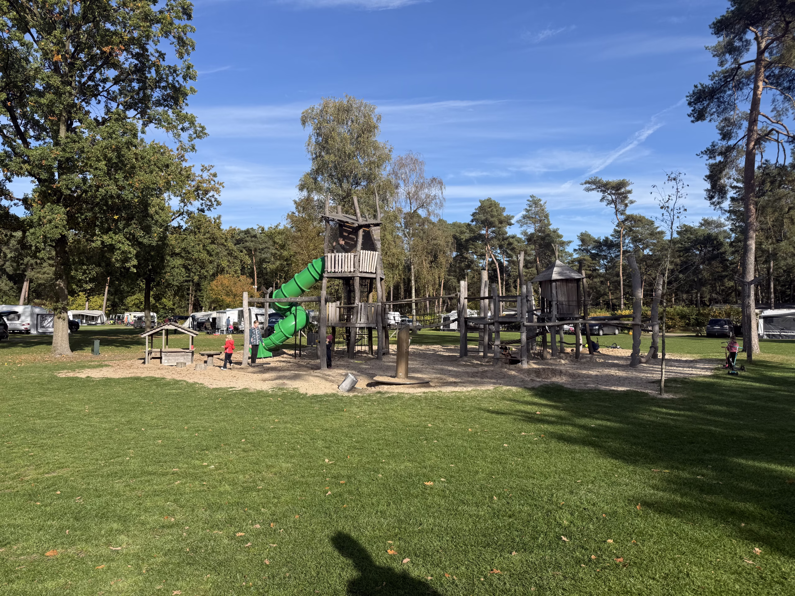 Groot houten speeltoestel met groene buisglijbaan op het veld